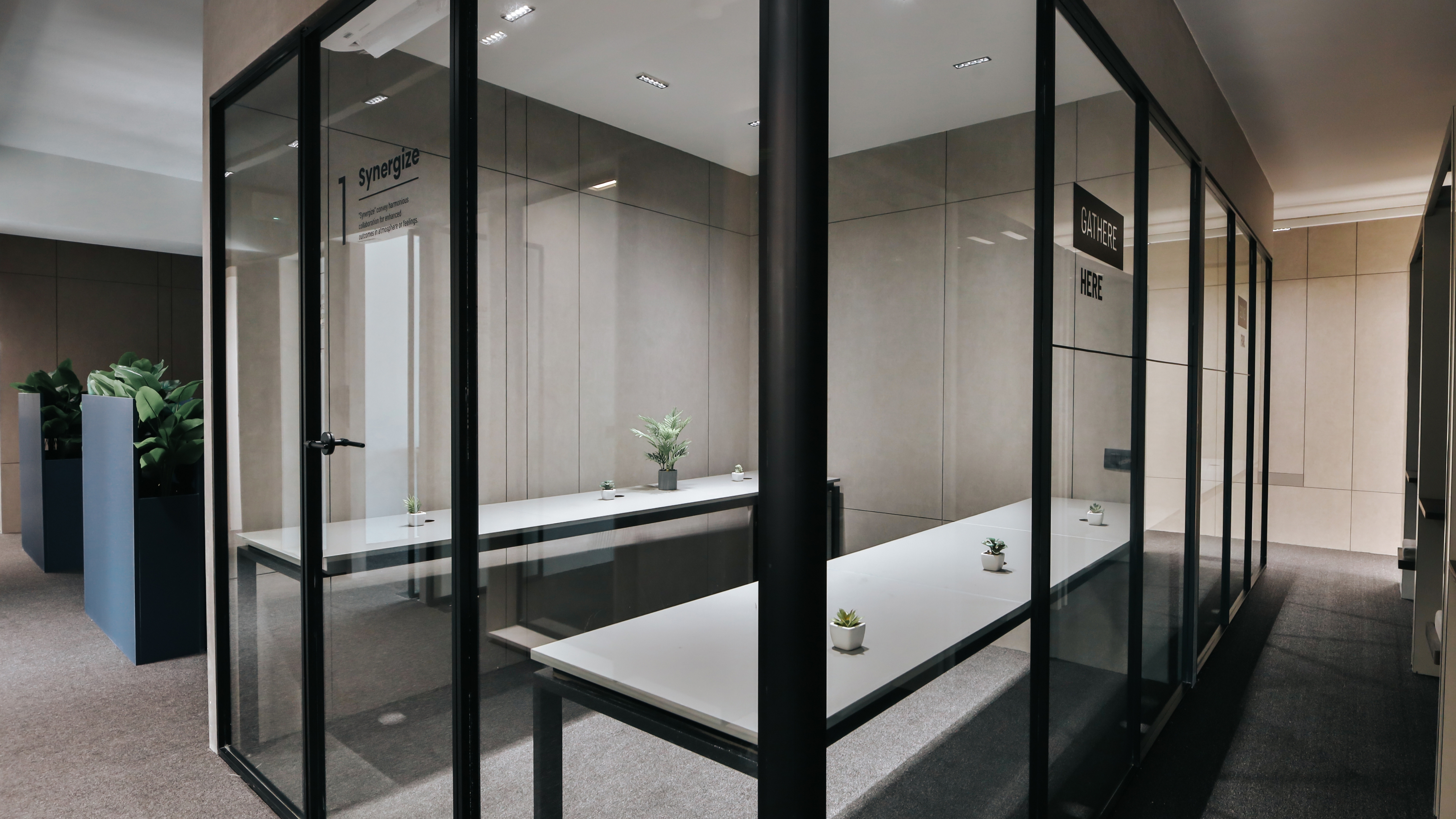 Modern glass-partitioned office meeting rooms with minimalist desks, indoor plants, and a clean, contemporary workspace design.