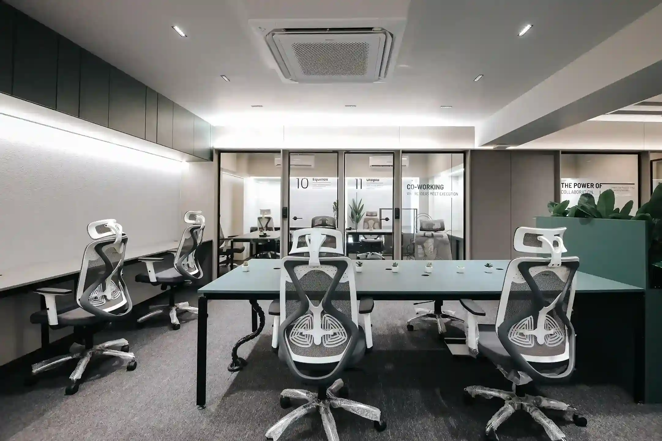 Modern shared office space with ergonomic chairs, long work desks, glass meeting rooms, and a clean minimalist startup workspace environment.