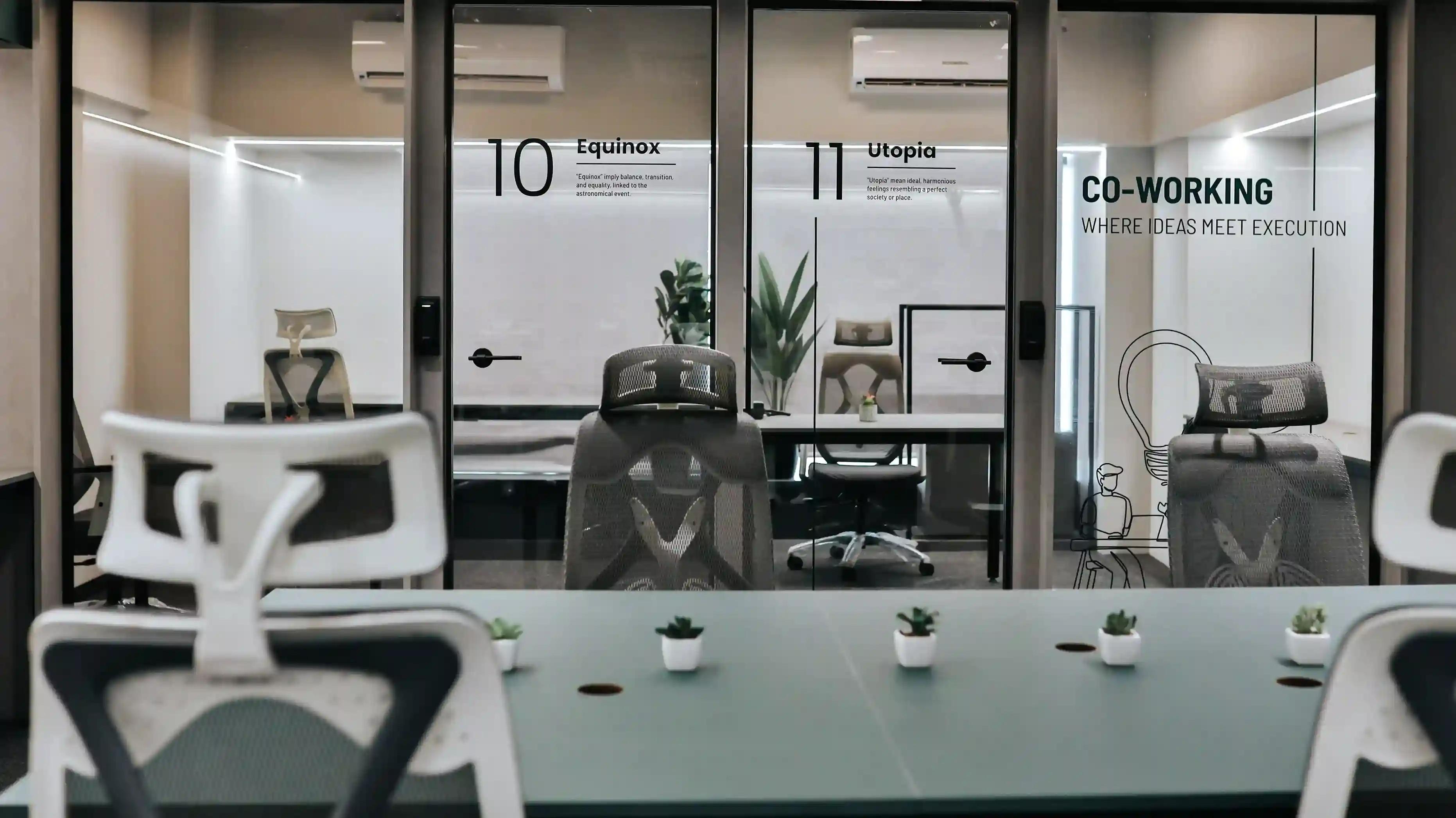 Modern coworking space in Gujarat featuring glass meeting rooms, ergonomic office chairs, minimalist interior design, and branding text on walls saying “Co-Working Where Ideas Meet Execution.”