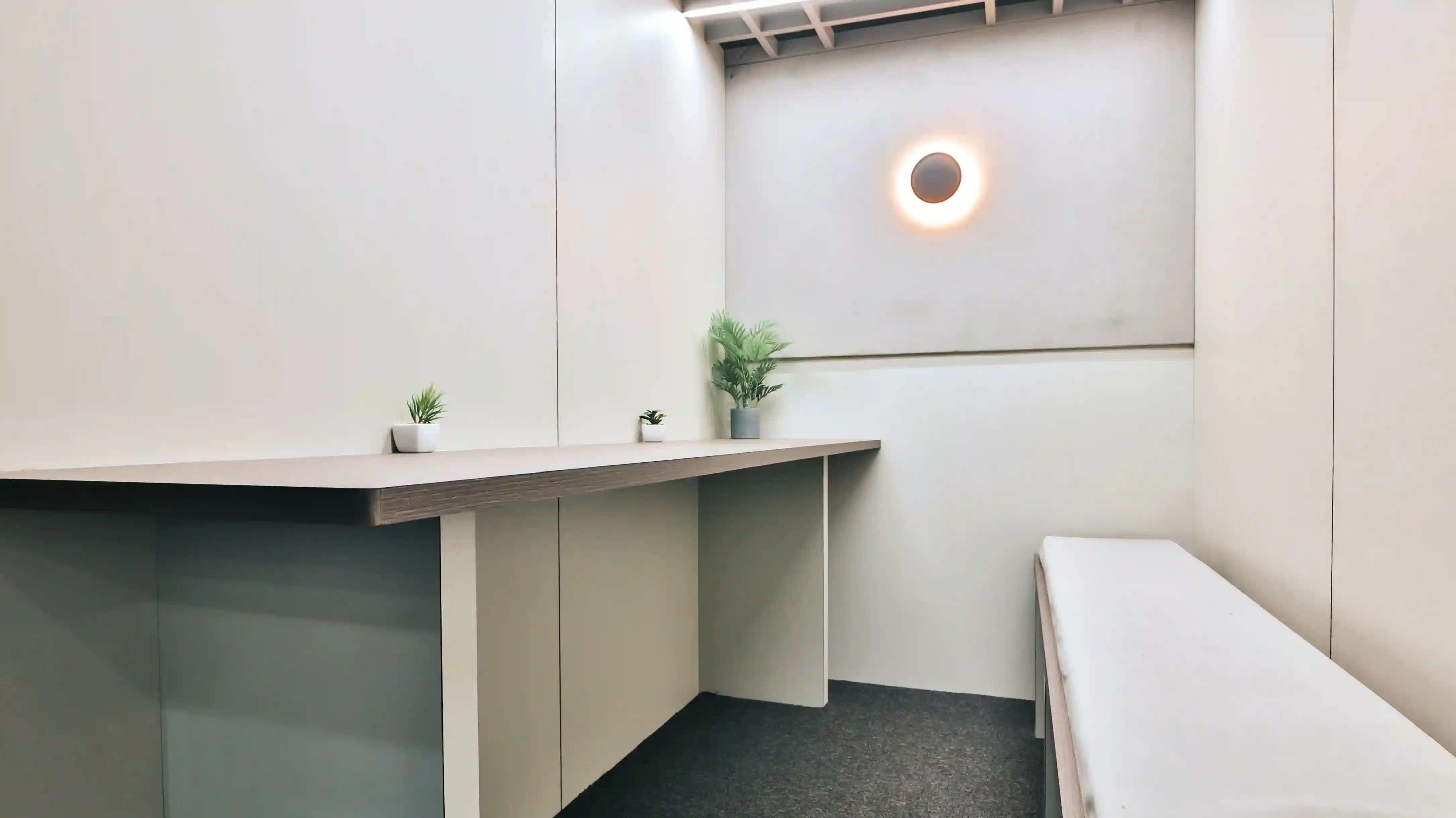 Minimalist coworking focus room with a long wooden desk, indoor plants, soft wall lighting, and a clean modern design ideal for deep work and quiet productivity.