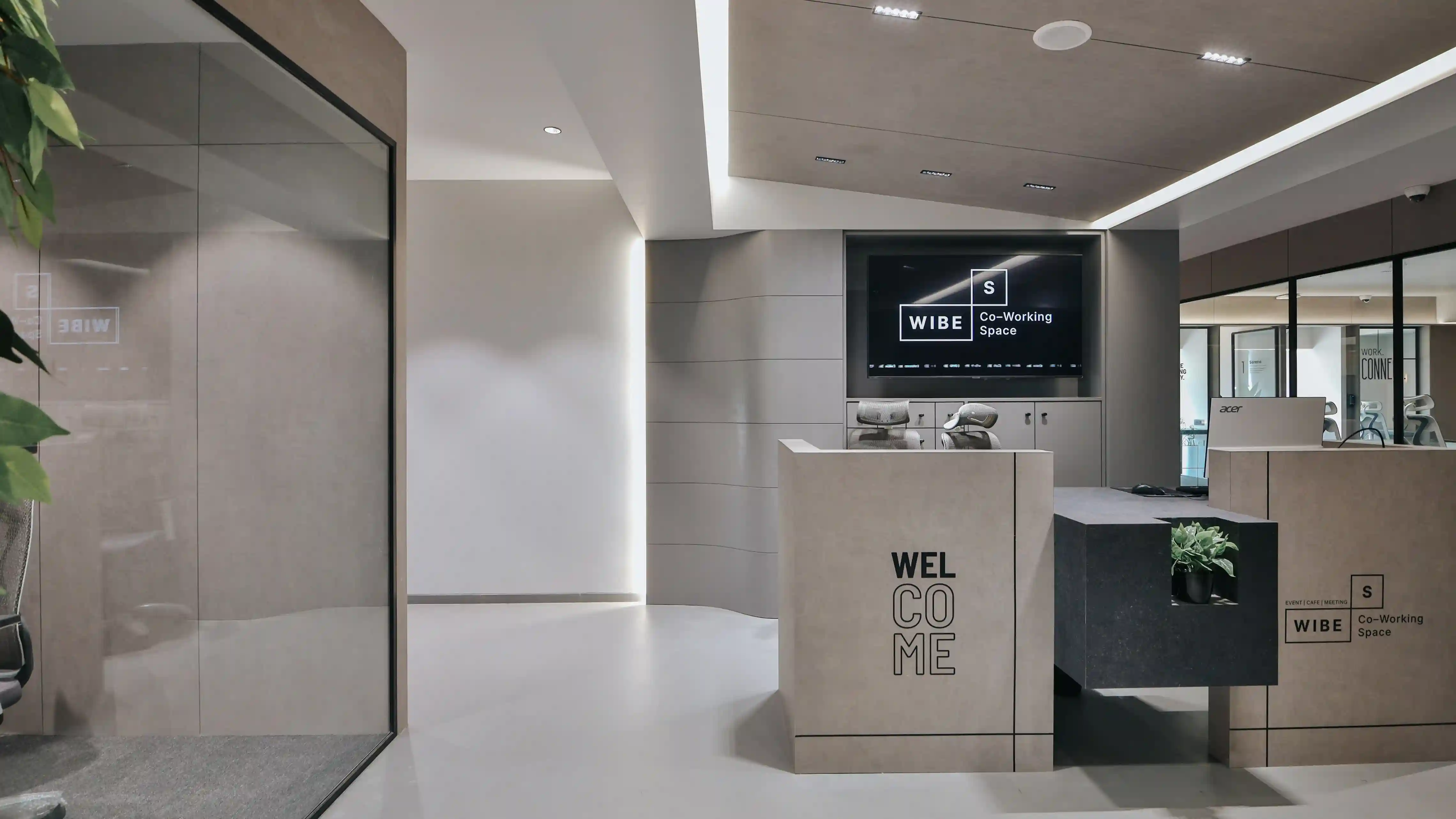 “Modern Wibes coworking space reception area with branded front desk, minimalist interior design, and professional meeting room entrance.”