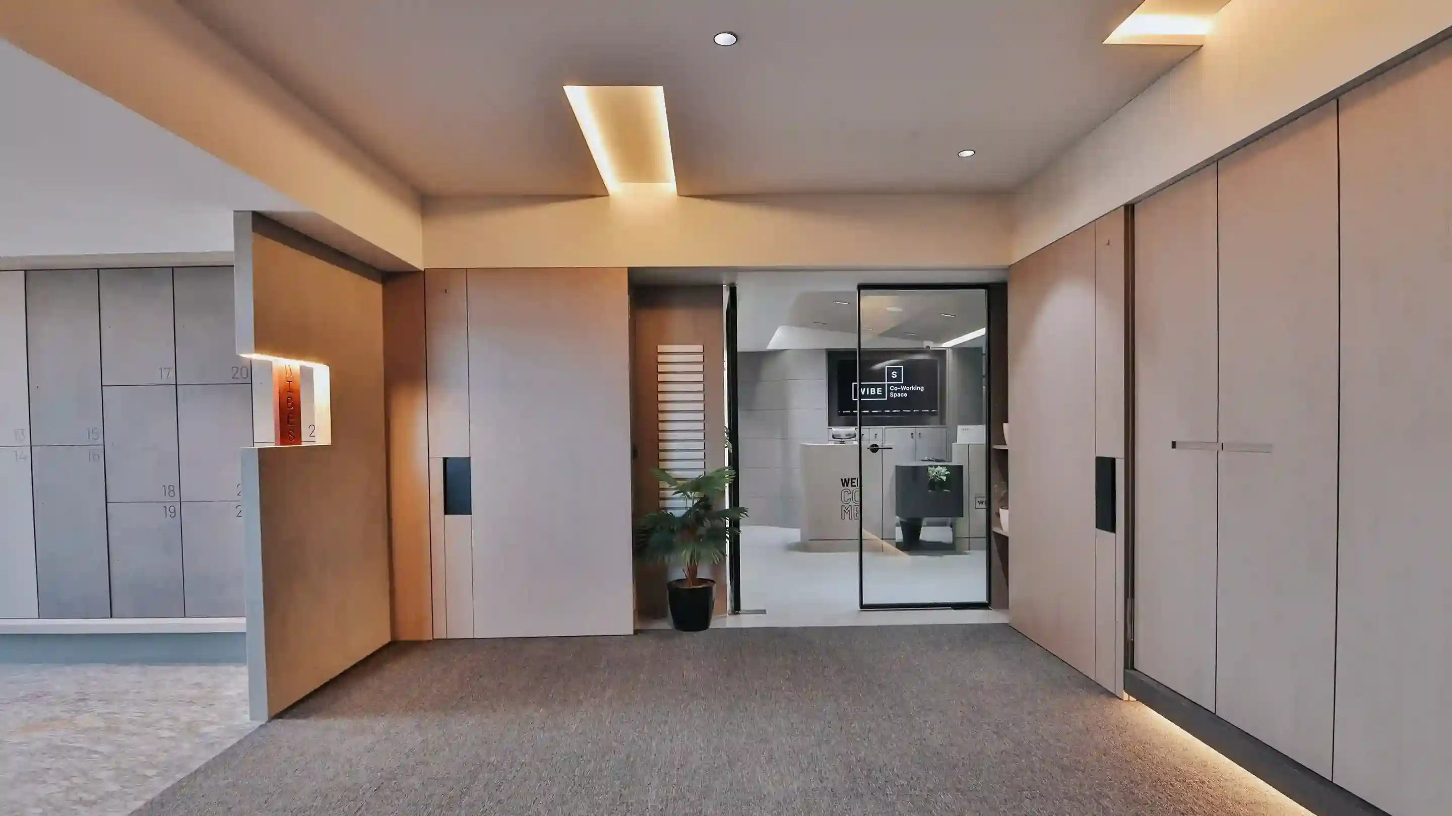 Contemporary coworking space interior with private meeting rooms, glass doors, warm lighting, and professional workspace layout.