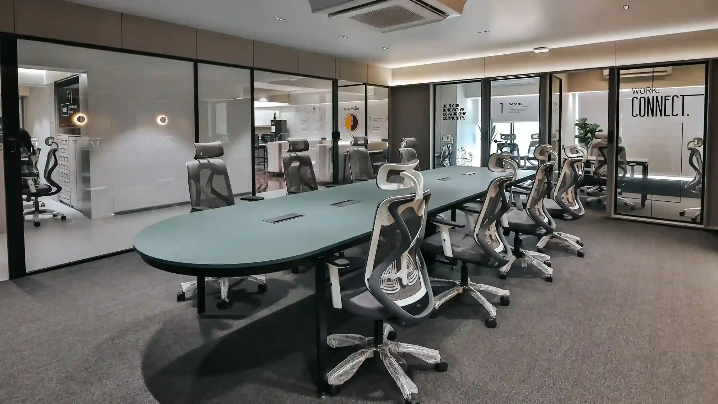 Contemporary office meeting room with a large conference table, ergonomic chairs, glass-walled rooms, and modern lighting, designed for collaborative work and team discussions in a coworking environment.
