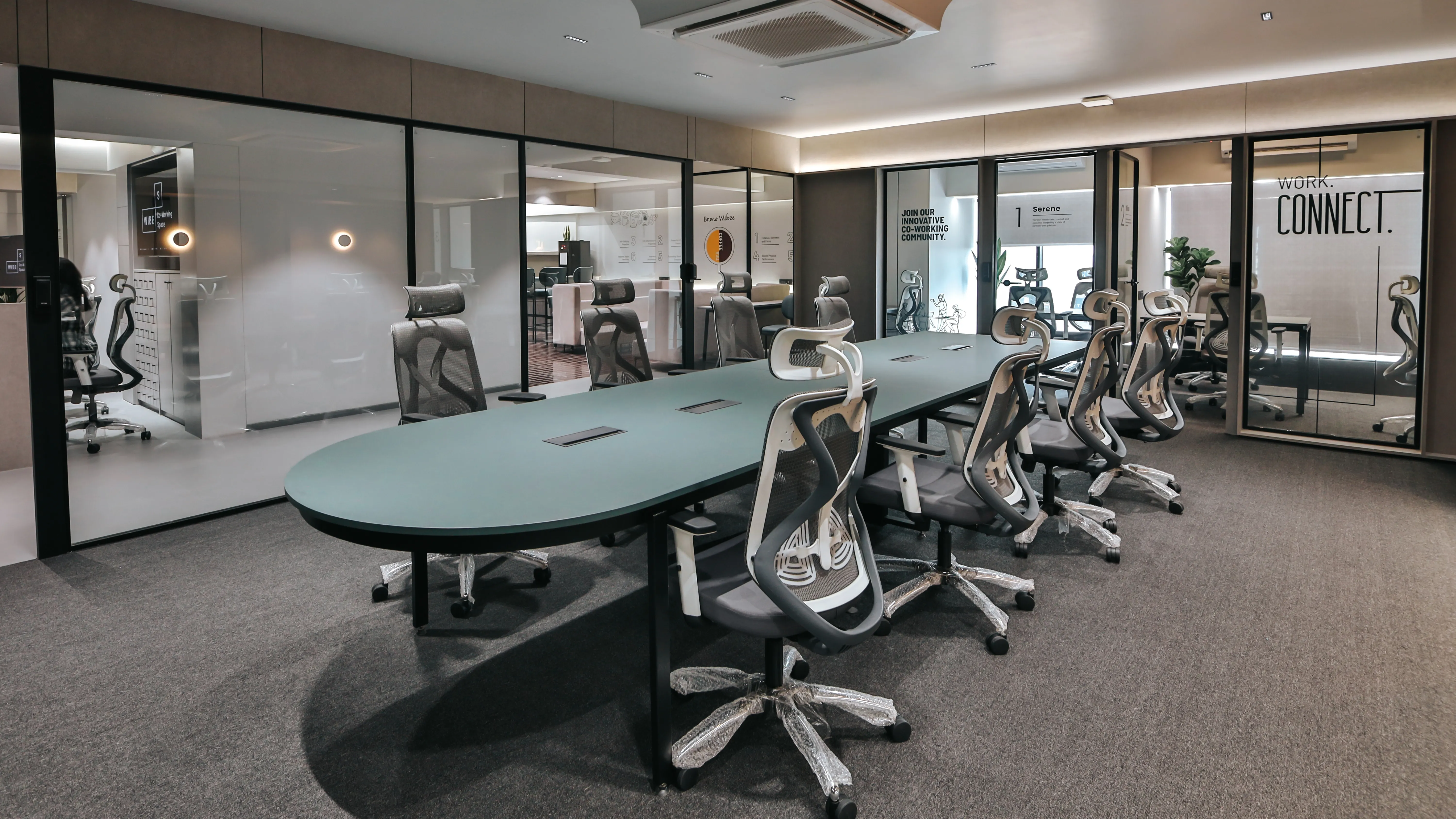 Modern coworking conference room with glass meeting cabins, ergonomic office chairs, long oval table, and minimal interior design with soft lighting.