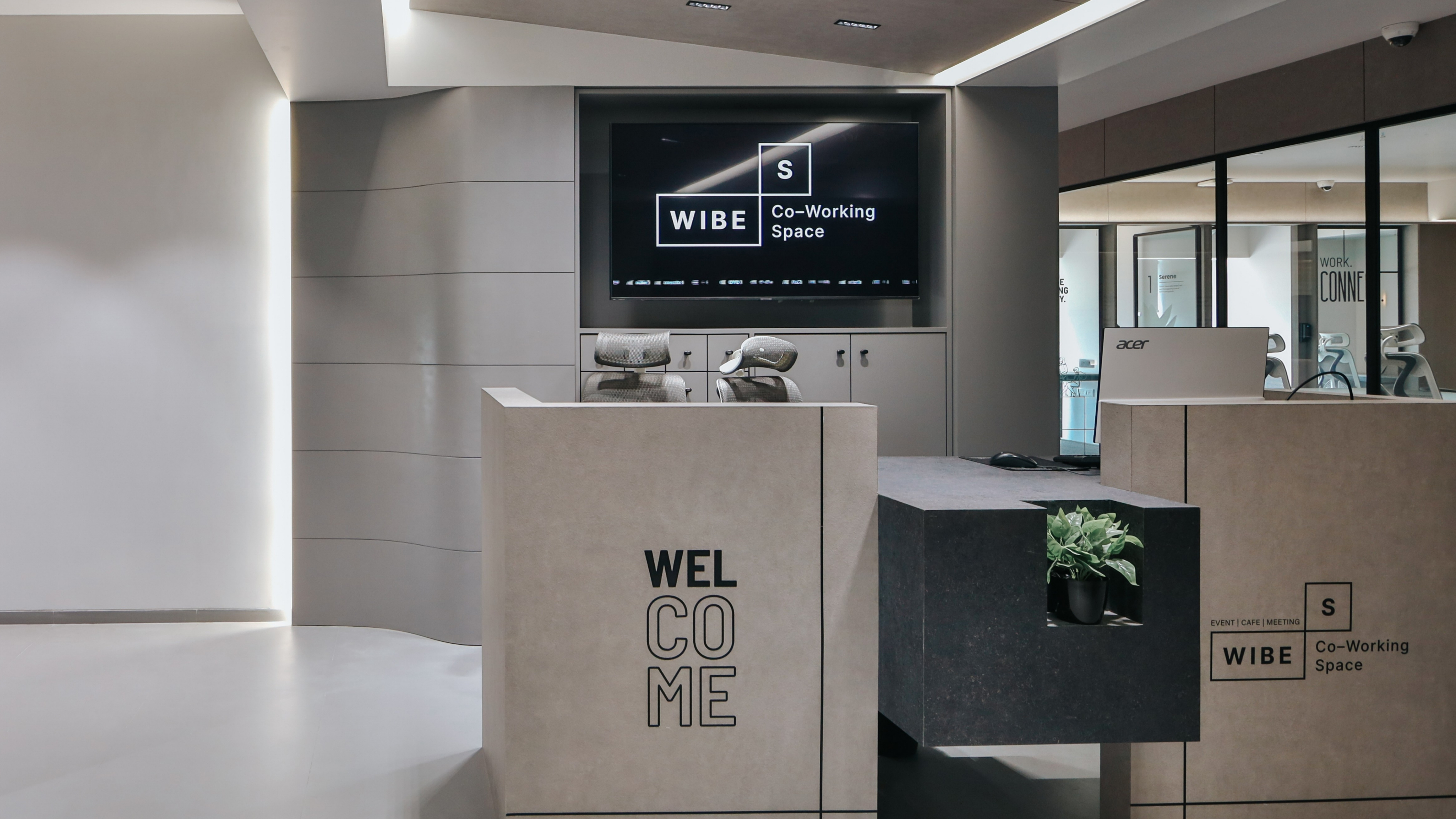 Modern coworking space reception desk with “Welcome” signage, Wibe Co-Working Space branding, digital display screen, and minimalist office interior.