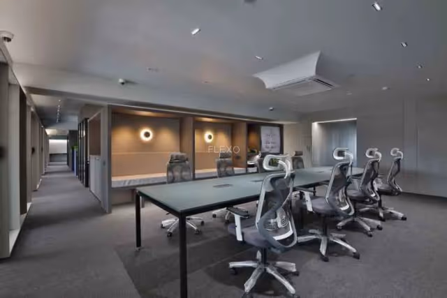 Modern coworking office with a long conference table, ergonomic office chairs, glass partitions, and warm ambient lighting, designed for professional meetings and collaborative work.