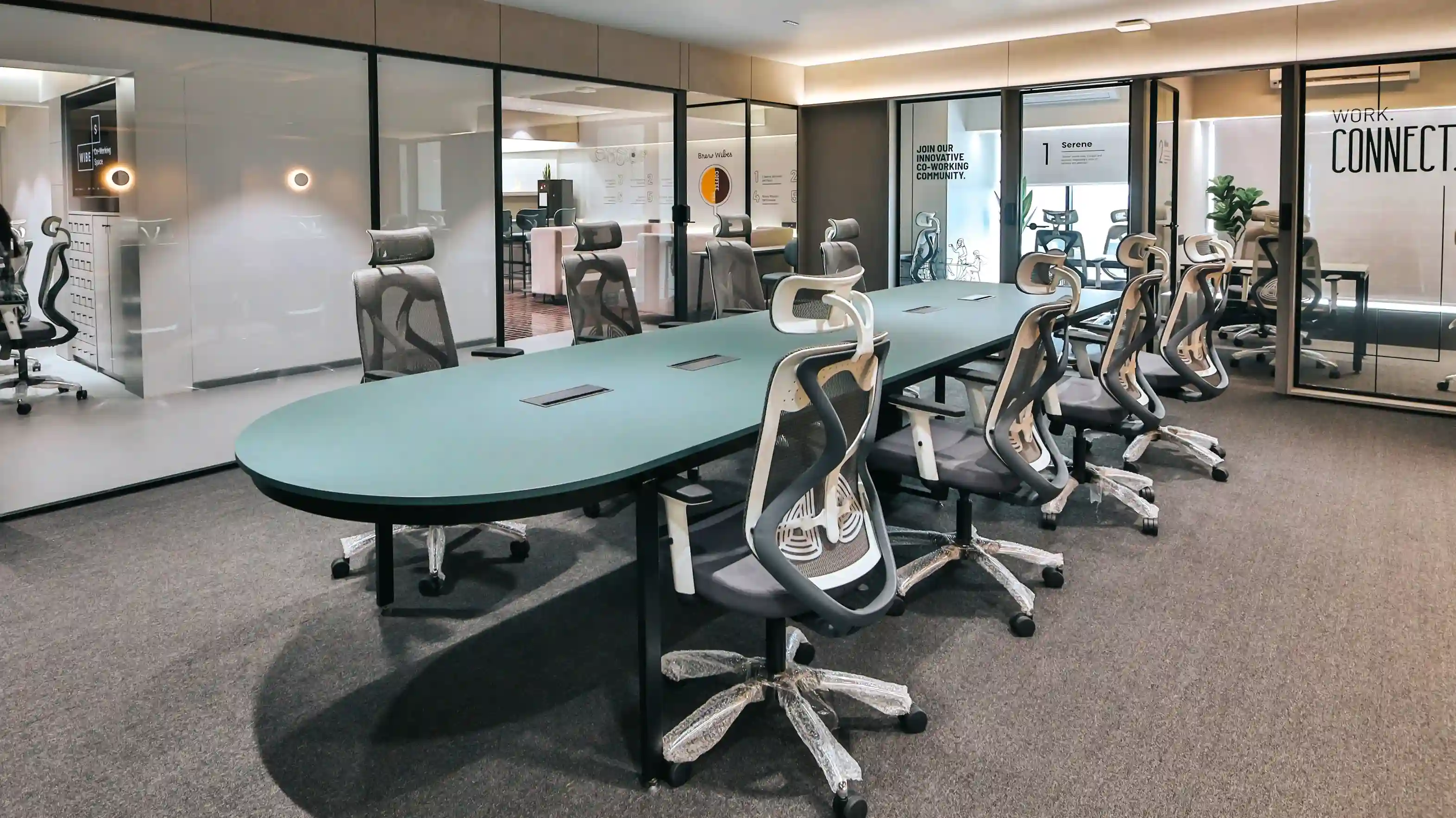 Modern coworking office featuring a long teal conference table, ergonomic mesh chairs, glass-walled meeting rooms, warm ceiling lighting, and a professional collaborative workspace with contemporary interior design.