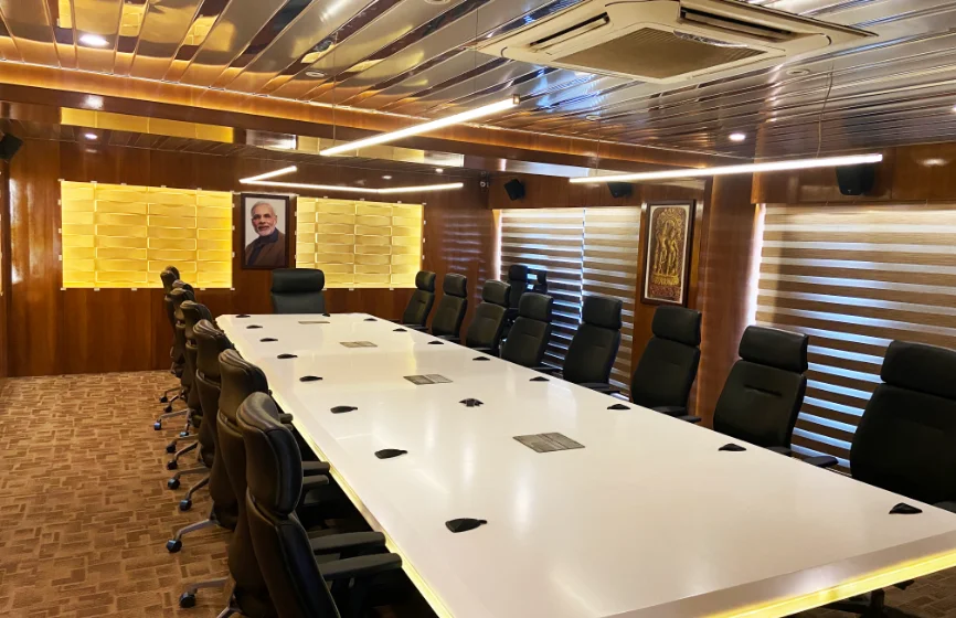 Luxurious corporate conference room with a long white meeting table, black executive chairs, wood-paneled walls, warm lighting, and window blinds.